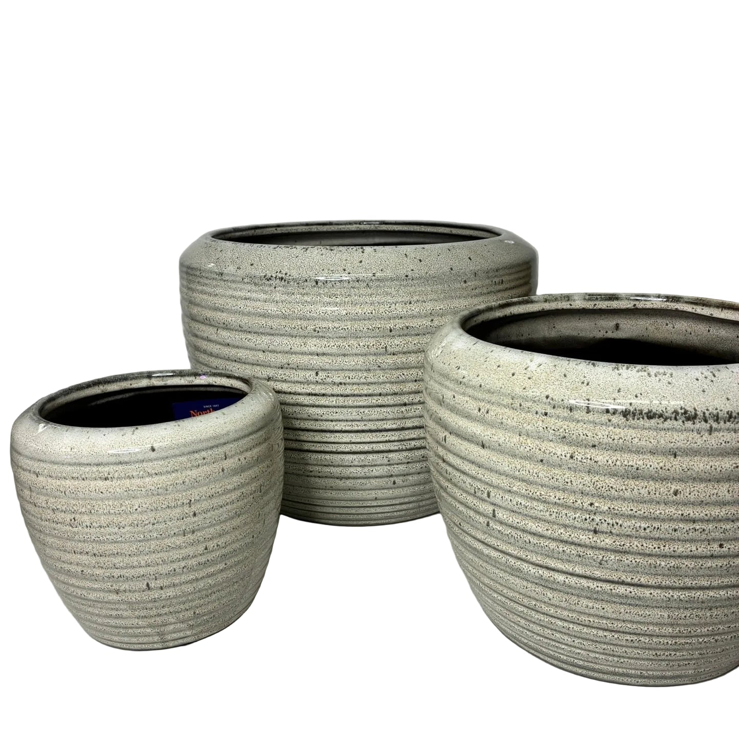 Three round ceramic planters in graduated sizes with a speckled light gray and white glaze, featuring horizontal ribbed texture and dark interior rims, displayed on a white surface against a light gray wall.